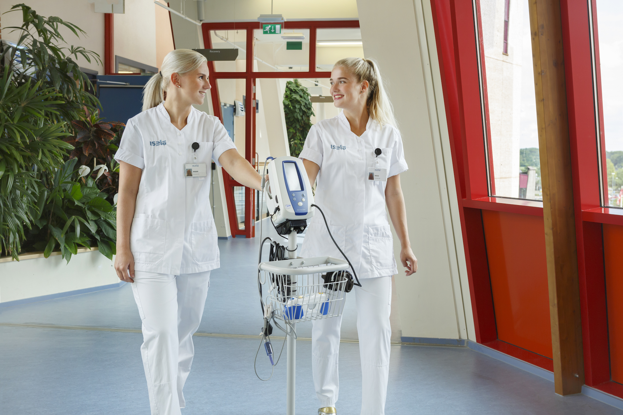 Twee verpleegkundigen lopen met een bloeddrukmeter door de gang Twee verpleegkundigen lopen met een bloeddrukmeter door de gang